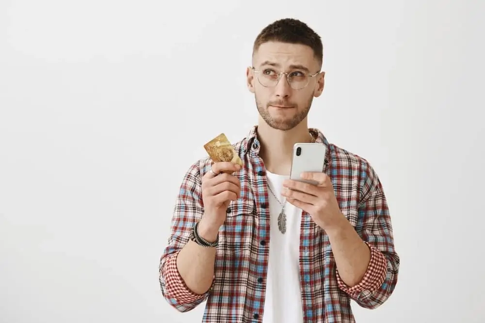 Jeune investisseur hésitant entre différentes options de plateformes crypto avec carte bancaire et smartphone